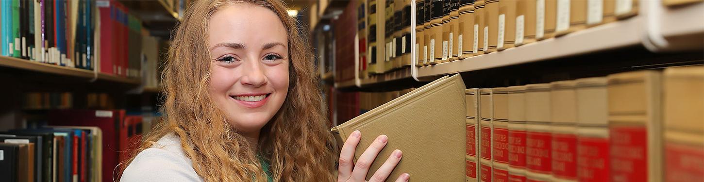 bet36365体育 student takes a book of a library shelf