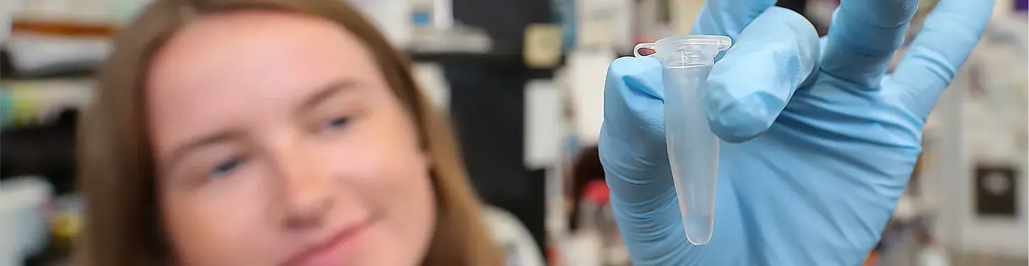 A student holds a vial in a gloved h和